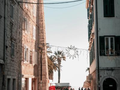 A bustling pedestrian walkway in Split, Croatia, featuring historic stone buildings and palm trees under a clear sky.