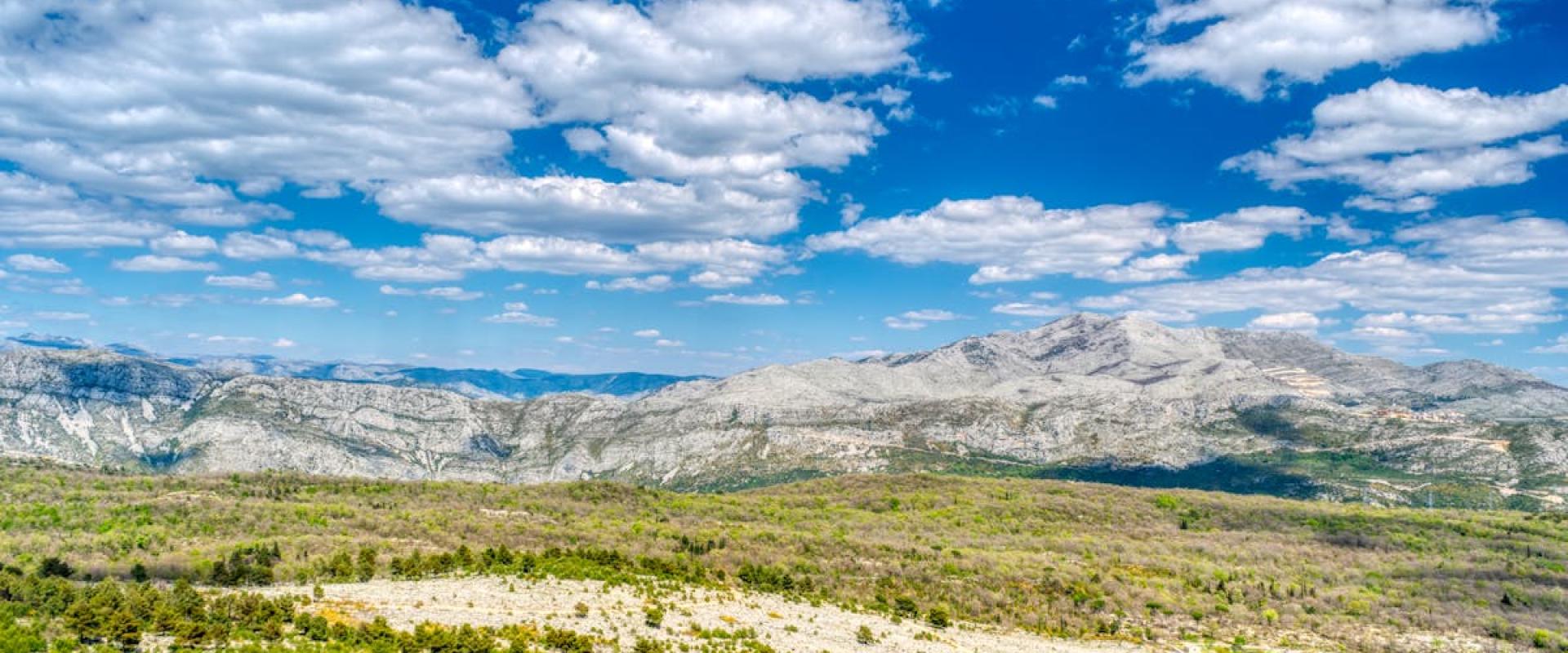 Scenic aerial view of mountains and fields under a bright blue sky in Dalmatia, Croatia.