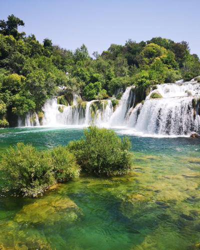 Scenic view of a lush waterfall in Krka National Park, Croatia, surrounded by vibrant greenery.