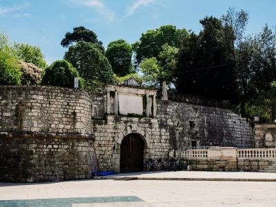 Explore the ancient stone gateway in Queen Jelena Madijevka Park, Zadar, with vibrant greenery and clear skies.