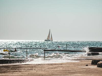 Free A tranquil view of a sailing boat on the shimmering sea under a clear sky, perfect for travel and leisure themes. Stock Photo