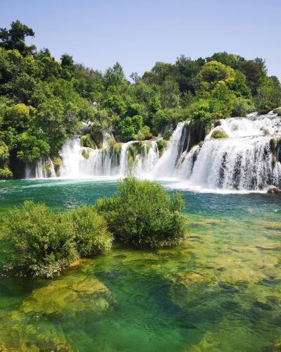 Scenic view of a lush waterfall in Krka National Park, Croatia, surrounded by vibrant greenery.