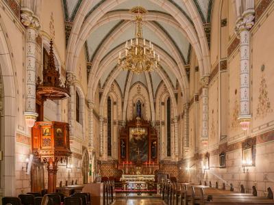 The interior of a church featuring Gothic Revival vaulted ceilings, a wooden pulpit, and an altar with a large painting.