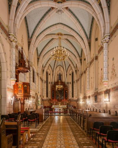 The interior of a church featuring Gothic Revival vaulted ceilings, a wooden pulpit, and an altar with a large painting.