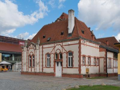 A white and red brick building with Gothic Revival architectural details, situated in a paved town square under a blue sky.