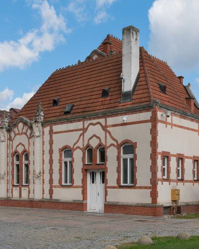 A white and red brick building with Gothic Revival architectural details, situated in a paved town square under a blue sky.