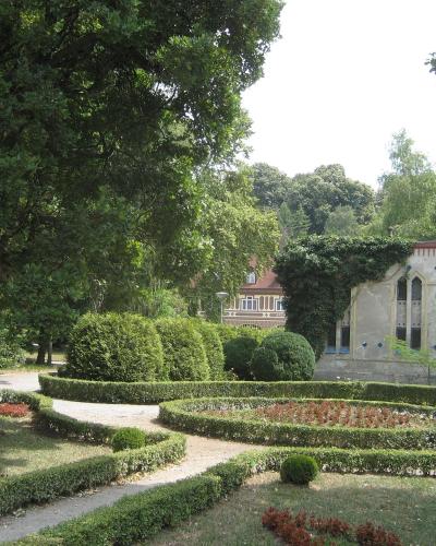 A manicured garden with low hedges and flowerbeds in the foreground, with a historic building featuring a dome and Moorish-style architectural details visible in the background amidst trees.