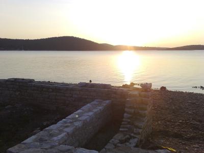 Low stone ruins of an ancient structure situated on a pebble beach next to the sea during sunset.