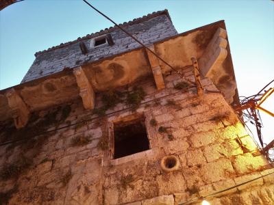 A low-angle shot of an old, weathered stone tower with a projecting upper floor supported by carved corbels, illuminated by warm artificial light against a twilight sky.
