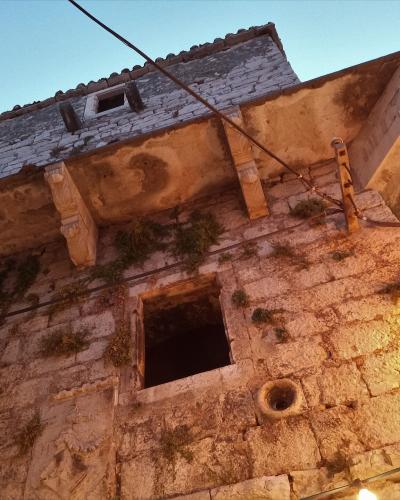 A low-angle shot of an old, weathered stone tower with a projecting upper floor supported by carved corbels, illuminated by warm artificial light against a twilight sky.