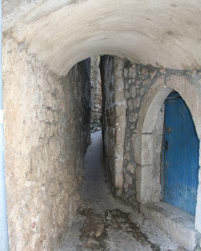 A narrow stone alleyway with a vaulted ceiling, featuring a blue wooden door set into an arched opening on the right side.