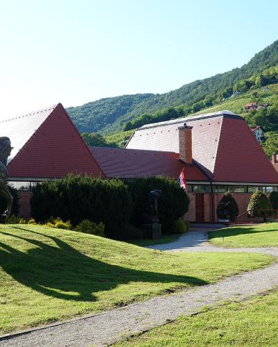 A large bronze horse statue stands on a grassy slope in front of a modern building with a distinctive red-tiled, angular roof, set against a backdrop of green hills.