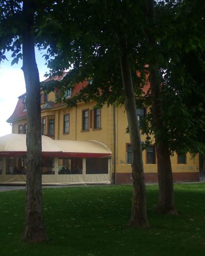 A yellow two-story building with a red-tiled roof, partially obscured by trees, with a large beige outdoor tent structure in front bearing the word "DVORAC" on its awning.