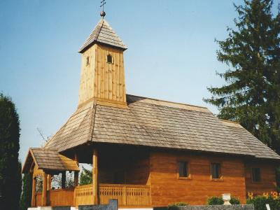 An 18th-century wooden chapel with a shingled roof and bell turret among pine trees, Lipik