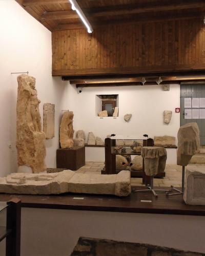 The interior of a museum room displaying ancient stone artifacts, including inscriptions, statues, and architectural fragments, under a wooden ceiling.