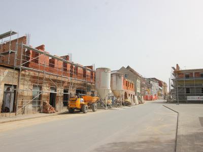 A street scene showing buildings under reconstruction with scaffolding, construction equipment, and silos, featuring a banner on the right that reads "GRAD PETRINJA SA".