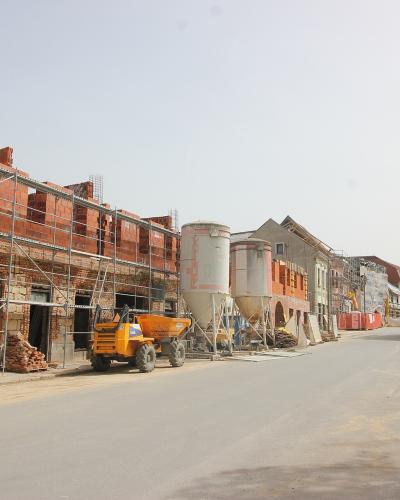 A street scene showing buildings under reconstruction with scaffolding, construction equipment, and silos, featuring a banner on the right that reads "GRAD PETRINJA SA".