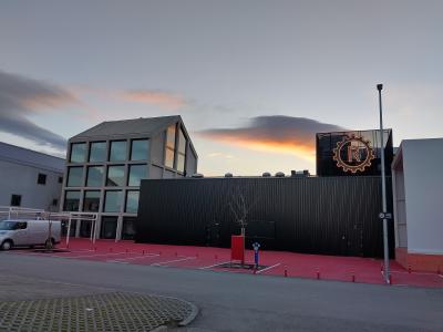 A modern building complex with a black corrugated metal facade and a distinctive illuminated gear-shaped logo containing the letter 'R' on the roof, set against a twilight sky.