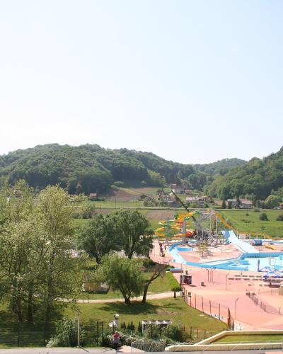 A wide-angle view of a large outdoor thermal water park featuring multiple colorful water slides, swimming pools, and surrounding green hills with scattered houses.