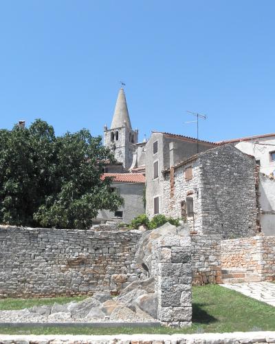 A view of the historic stone town of Bale in Croatia, featuring old stone buildings, a prominent church tower with a conical roof, and a stone wall in the foreground.
