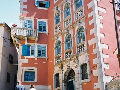A tall, salmon-pink building with white quoins and blue shutters, featuring a grand stone staircase leading up to an arched entrance, with the word "MUSEUM" carved into the stone facade near the ground floor.