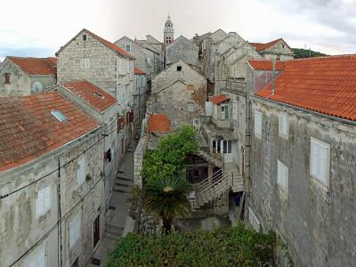 A panoramic view from an elevated position overlooking the narrow streets, stone buildings with terracotta roofs, and the sea of the Old Town of Korčula, Croatia.