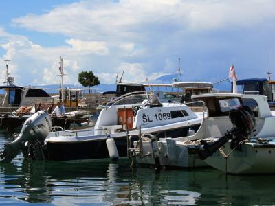 A daytime view of several small motorboats and fishing vessels moored in a harbor, with a person visible on a dock in the background.