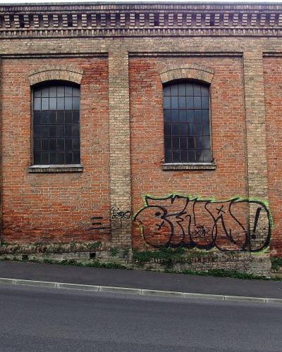 A red brick building facade with four arched windows, graffiti on the lower wall, and a white sign reading "GLIPTOTEKA" with a logo above it.