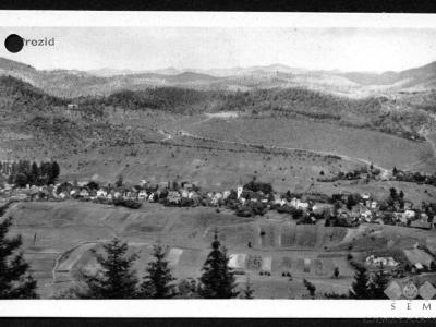 A vintage black-and-white postcard showing a panoramic view of a small village nestled in a valley surrounded by forested hills, with the text "Prezid" printed in the upper left corner and "S E M" in the lower right.