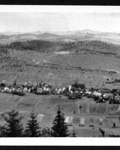 A vintage black-and-white postcard showing a panoramic view of a small village nestled in a valley surrounded by forested hills, with the text "Prezid" printed in the upper left corner and "S E M" in the lower right.
