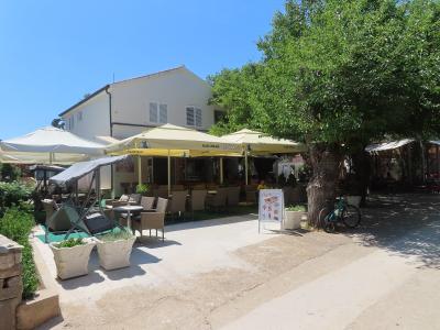 An outdoor restaurant patio with yellow umbrellas, tables, and chairs, featuring a white A-frame sign with the name "Oaza" and a bicycle parked under a tree.