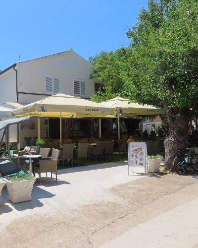 An outdoor restaurant patio with yellow umbrellas, tables, and chairs, featuring a white A-frame sign with the name "Oaza" and a bicycle parked under a tree.